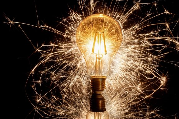 Glühbirne, umgeben von funkelnden Lichtspliter und Strahlen auf schwarzem Hintergrund.